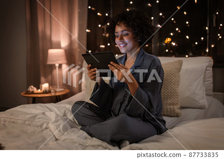 happy woman with tablet pc sitting in bed at night happy woman with tablet pc sitting in bed at night 87733835