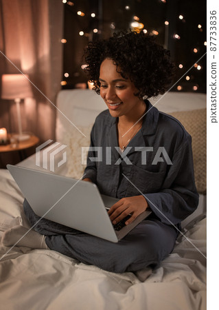 happy woman with laptop sitting in bed at night 87733836