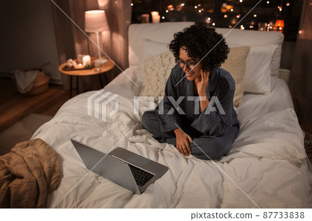 happy woman with laptop sitting in bed at night happy woman with laptop sitting in bed at night 87733838