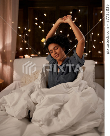 sleepy woman stretching in bed at night sleepy woman stretching in bed at night 87733839
