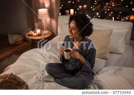 happy woman with hot chocolate sitting in bed 87733840