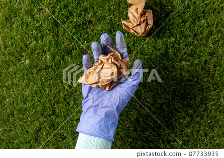 close up of hand in glove picking paper waste close up of hand in glove picking paper waste 87733935