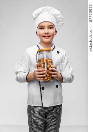 smiling boy in chef's toque holding jar with pasta smiling boy in chef's toque holding jar with pasta 87733936