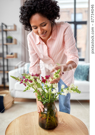 happy woman placing flowers on table at home happy woman placing flowers on table at home 87734046