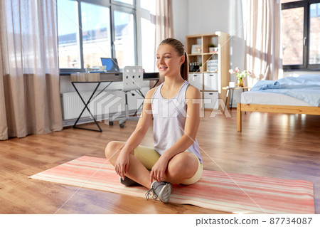 smiling teenage girl sitting on yoga mat at home smiling teenage girl sitting on yoga mat at home 87734087