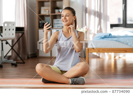 girl with phone and earphones exercising at home girl with phone and earphones exercising at home 87734090