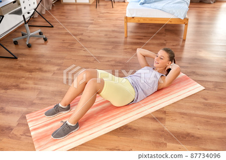 happy teenage girl exercising on yoga mat at home happy teenage girl exercising on yoga mat at home 87734096