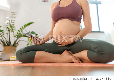 close up of pregnant woman with phone doing yoga 87734119