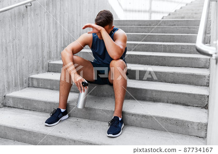 tired sportsman with bottle sitting on city bench 87734167