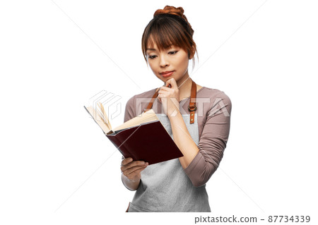 thinking woman in apron reading cook book thinking woman in apron reading cook book 87734339