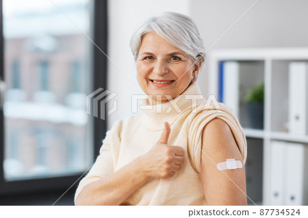 smiling vaccinated woman with medical patch on arm 87734524