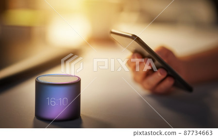 hand with smartphone and time on smart speaker hand with smartphone and time on smart speaker 87734663