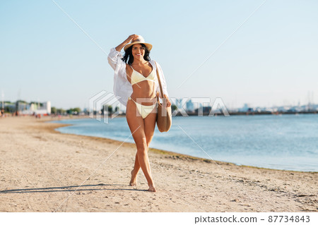 happy woman in bikini and shirt walking on beach happy woman in bikini and shirt walking on beach 87734843