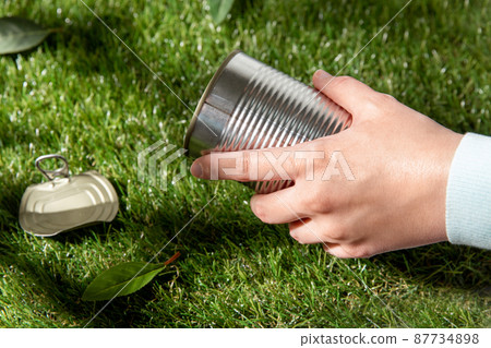 close up of hand removing used tin can from grass 87734898