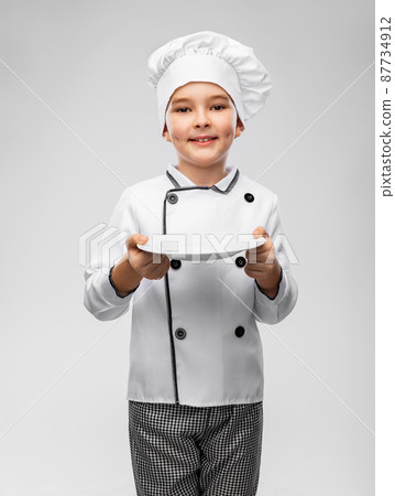 smiling boy in chef's toque holding empty plate 87734912