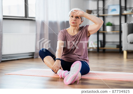 tired senior woman exercising on mat at home tired senior woman exercising on mat at home 87734925