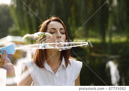 Woman blow a soap bubbles while standing in a park Woman blow a soap bubbles while standing in a park 87735082