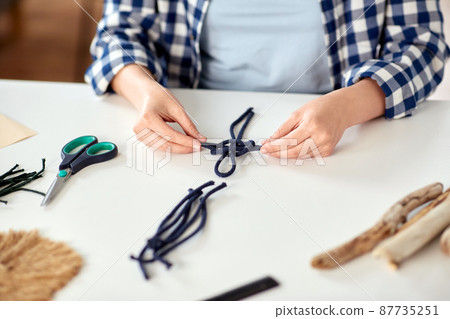 woman making macrame and knotting cords 87735251