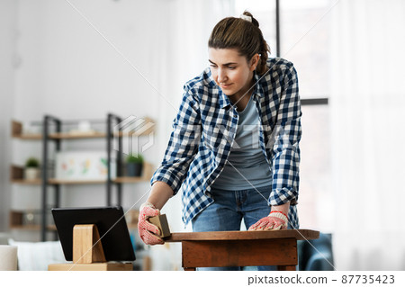 woman sanding old round wooden table with sponge 87735423