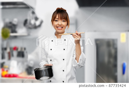 female chef with saucepan tasting food on kitchen 87735424