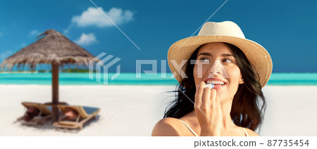 smiling woman in bikini with lip balm on beach 87735454
