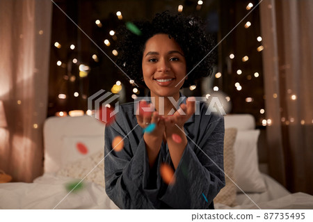 woman blowing confetti in bed at night at home 87735495