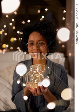 woman with garland in glass mug in bed at night 87735504