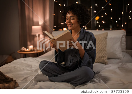 happy woman reading book sitting in bed at night happy woman reading book sitting in bed at night 87735509