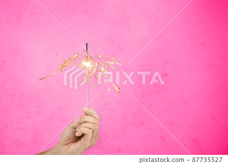 hand with sparkler burning over pink background hand with sparkler burning over pink background 87735527