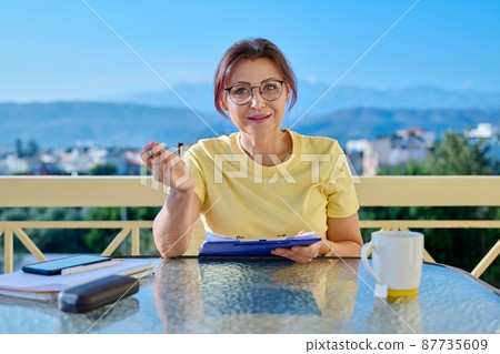 Portrait of business woman looking at webcam while sitting at home office desk Portrait of business woman looking at webcam while sitting at home office desk 87735609