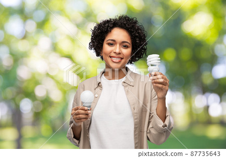 smiling woman holding lighting bulbs over green 87735643