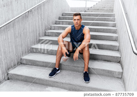 sportsman with shake in bottle sitting on stairs 87735709