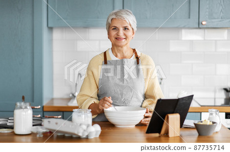 happy woman with cook book cooking food on kitchen 87735714