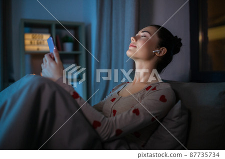 happy teenage girl with phone and earphones in bed happy teenage girl with phone and earphones in bed 87735734