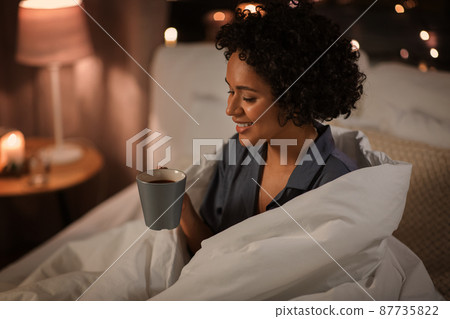 happy woman with coffee sitting in bed at night happy woman with coffee sitting in bed at night 87735822