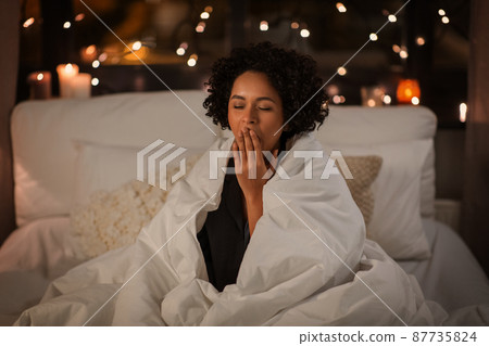 yawning woman wrapped in blanket in bed at night yawning woman wrapped in blanket in bed at night 87735824