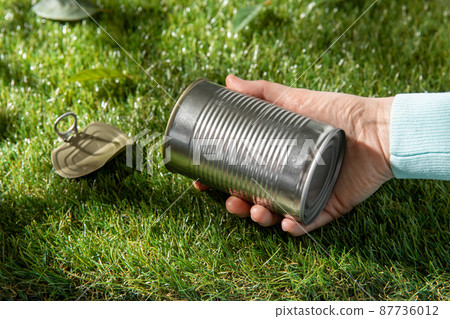 close up of hand removing used tin can from grass 87736012