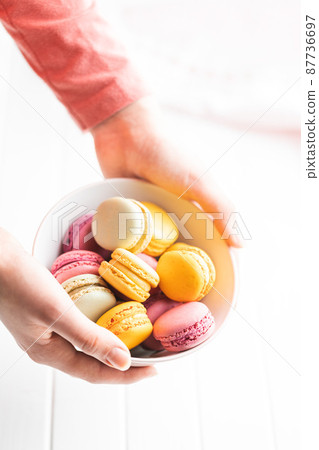 Sweet colorful macarons. Traditional french macaroons. Tasty dessert in bowl held in hands 87736697