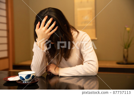 A woman holding her head at an inn worries 87737113