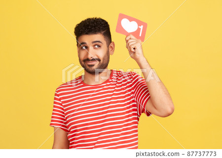 Dreamy bearded man blogger holding above head red like counter sign, asking for more reactions on his content in social media. Indoor studio shot isolated on yellow background Dreamy bearded man blogger holding above head red like counter sign, asking for more reactions on his content in social media. Indoor studio shot isolated on yellow background 87737773