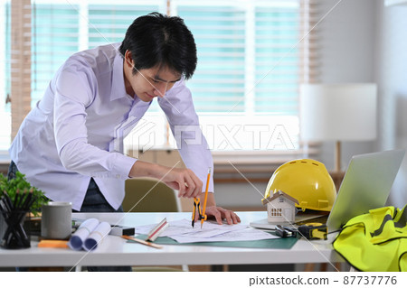 Asian male construction engineer working with blueprint in office. Asian male construction engineer working with blueprint in office. 87737776
