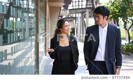 Two young business colleagues discussing business while walking outside office. Two young business colleagues discussing business while walking outside office. 87737894