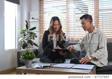 Asian young female insurance agent in formal suit offer life insurance to elderly man. Asian young female insurance agent in formal suit offer life insurance to elderly man. 87737897