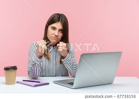 Angry annoyed woman in striped shirt sitting at laptop on workplace keeping fists clenched to punch, showing boxing gesture, ready to fight for job. Indoor studio shot isolated on pink background Angry annoyed woman in striped shirt sitting at laptop on workplace keeping fists clenched to punch, showing boxing gesture, ready to fight for job. Indoor studio shot isolated on pink background 87738158