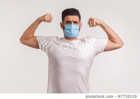 Man in hygienic mask showing strength and immunity to recover from contagious disease, airborne respiratory illness such as flu, coronavirus 2019-nCoV. indoor studio shot isolated on white background 87738319