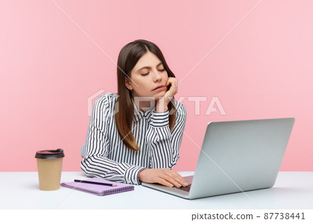 Bored unhappy business woman sitting at workplace looking at laptop display having video call, tired of online conference, procrastination. Indoor studio shot isolated on pink background 87738441