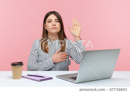 I swear. Honest dedicated woman office worker raising hand to give promise sitting at workplace, taking oath with trustworthy faithful expression. Indoor studio shot isolated on pink background 87738603