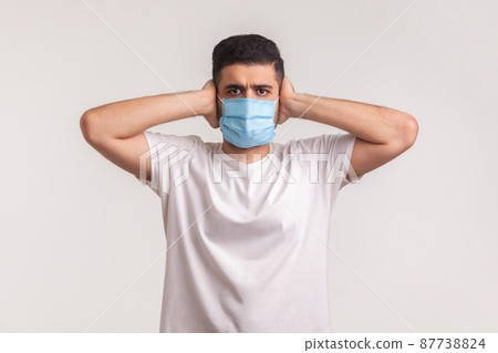 Protection against coronavirus, contagious disease. Man covering ears and wearing hygienic safety mask to prevent infection, respiratory illness such as flu, 2019-nCoV, ebola. studio shot, isolated Protection against coronavirus, contagious disease. Man covering ears and wearing hygienic safety mask to prevent infection, respiratory illness such as flu, 2019-nCoV, ebola. studio shot, isolated 87738824