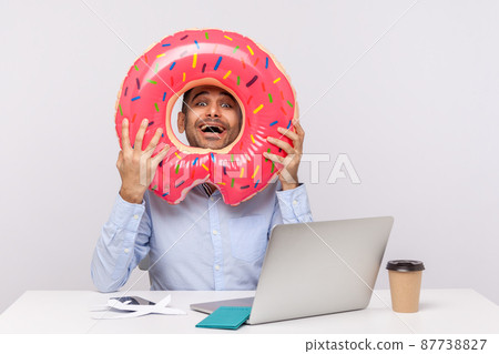 Extremely happy man looking through rubber ring and smiling excitedly, sitting in office workplace with passport on desk, celebrating planned travel vacation, weekend trip. studio shot isolated 87738827
