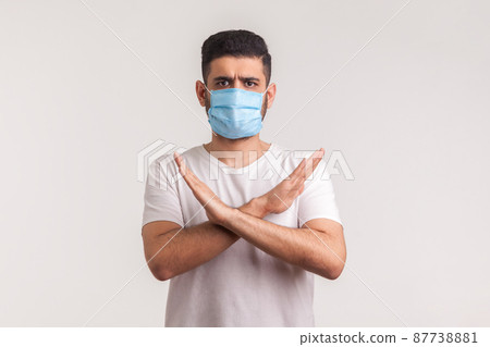 Man in protective hygienic mask standing with crossed arms, gesturing stop, warning of coronavirus epidemic, infection, respiratory diseases such as flu, 2019-nCoV, ebola. indoor studio shot, isolated Man in protective hygienic mask standing with crossed arms, gesturing stop, warning of coronavirus epidemic, infection, respiratory diseases such as flu, 2019-nCoV, ebola. indoor studio shot, isolated 87738881